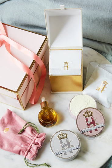 Open pink gift box with a serum bottle, a pink pouch, tins and a ribbon