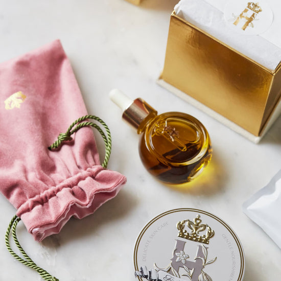 Pink pouch, a serum bottle, a First Touch tin and an open gift box on marble