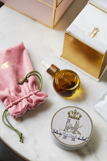 Pink pouch, a serum bottle, a First Touch tin and an open gift box on marble