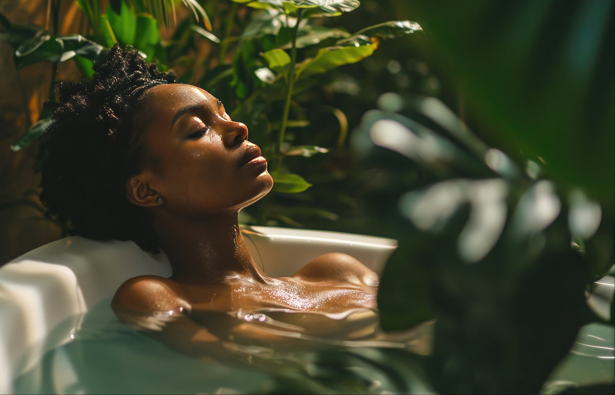 A woman relaxing in a white bathtub surrounded by lush green tropical plants, with warm, moody lighting highlighting her face and wet skin.