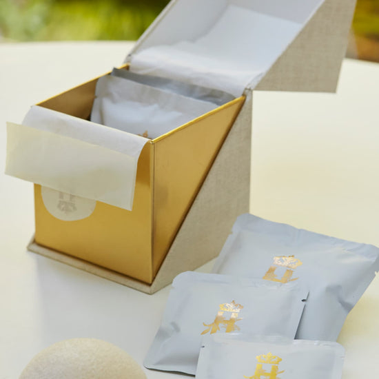 Open gold ritual box with soak sachets and a konjac sponge on a table outdoors
