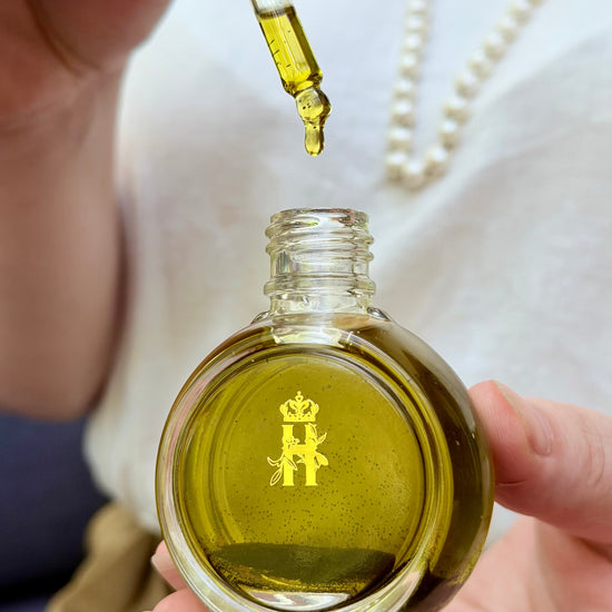Hand squeezing a dropper over a round glass serum bottle