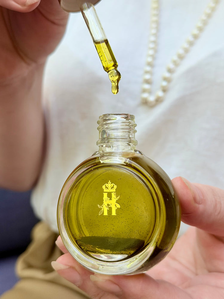 Hand squeezing a dropper over a round glass serum bottle