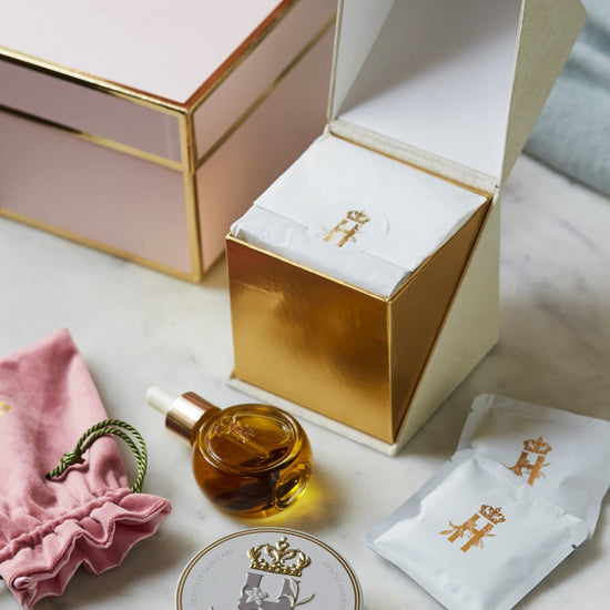 Open pink gift box beside a serum bottle, a pink pouch, a First Touch tin and soak sachets