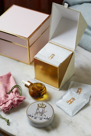 Open pink gift box beside a serum bottle, a pink pouch, a First Touch tin and soak sachets