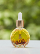 Royal Heir Botanicals Balancing Rose Facial serum in a round glass dropper bottle with a gold dropper top and a golden logo on the front face of the bottle photographed on a white surface against a blurry green foliage background.