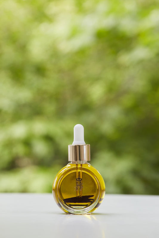Tender Skin Serum in a round glass bottle with a gold dropper, in front of green foliage